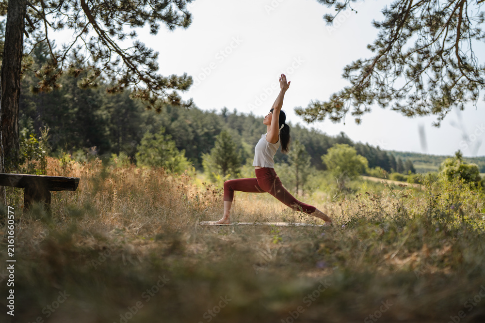 Naklejka premium Woman practicing yoga warrior pose in nature