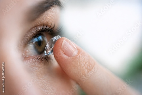 A close-up shot of a person's hand holding a contact lens, ready for application