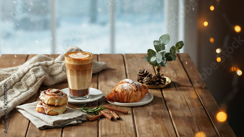 Latte with cinnamon rolls and croissant on a wooden table with festive lights during winter