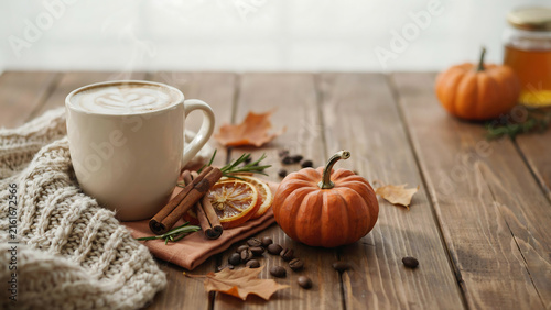 Steaming latte with pumpkin spice and cinnamon sticks on a rustic wooden table with autumn leaves and honey
