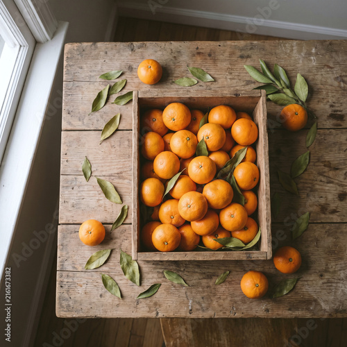 Freshly Harvested Mikan Mandarins Piled in Wooden Crate with Leaves, Overhead Flat Lay
