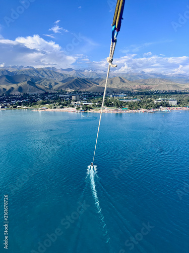 Aerial view from a parasail over Cholpon-Ata, Kyrgyzstan, in August, overlooking Lake Issyk-Kul and the dramatic mountain ranges surrounding its shores.