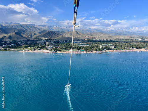 Aerial view from a parasail over Cholpon-Ata, Kyrgyzstan, in August, overlooking Lake Issyk-Kul and the dramatic mountain ranges surrounding its shores.