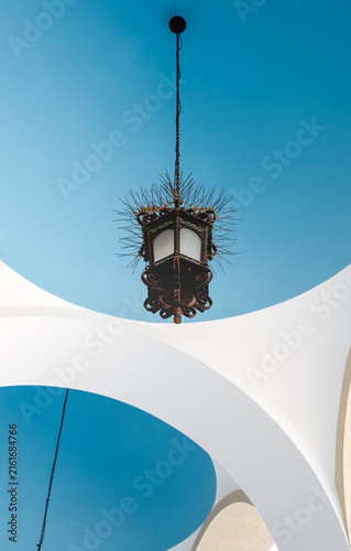 Hanging lantern suspended beneath a blue vaulted ceiling featuring modern architectural forms in Patras, Greece.