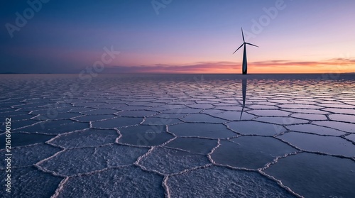 Modern wind turbine standing in vast salt flats reflecting sky at beautiful purple sunset.