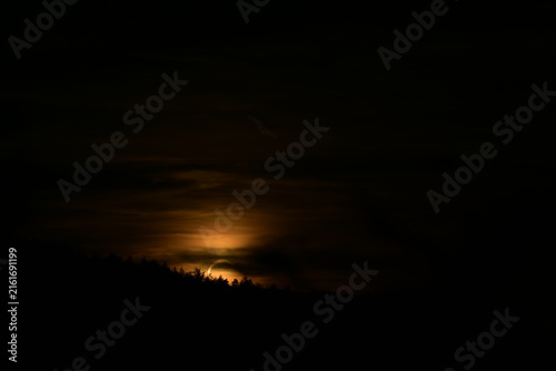Sonnenuntergang während einer partiellen Sonnenfinsternis hinter einem bewaldeten Hügel