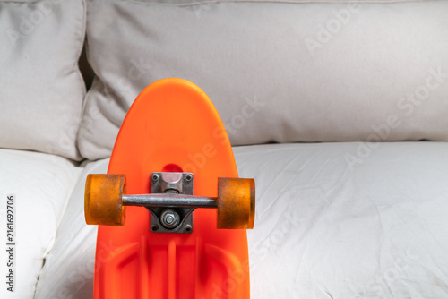 Konstfotografi Bright orange mini cruiser skateboard resting on couch, wheels and trucks, graph
