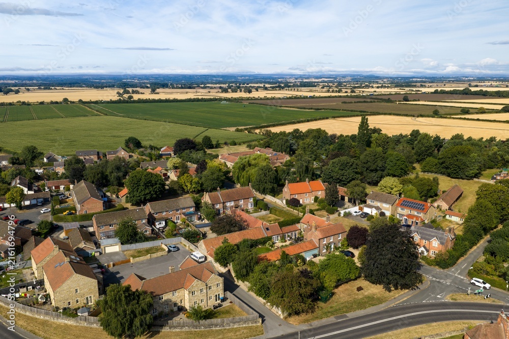Fototapeta premium Aerial photo overlooking traditional homes near Thirsk Yorkshire surrounded by expansive agricultural fields mature trees country roads and rolling North Yorkshire countryside in the distance