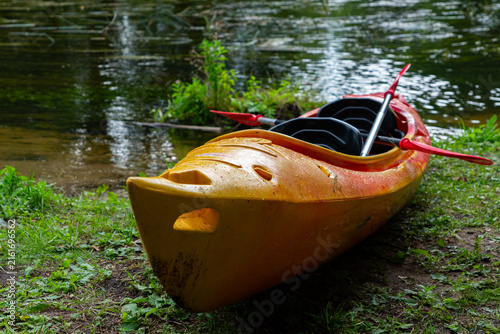 Konstfotografi Colorful yellow and orange kayak with paddles beside a forest stream, outdoor wa