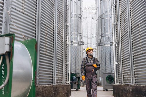 Fotografía Male farmer inspecting agro silos at a granary, walking between metal grain stor
