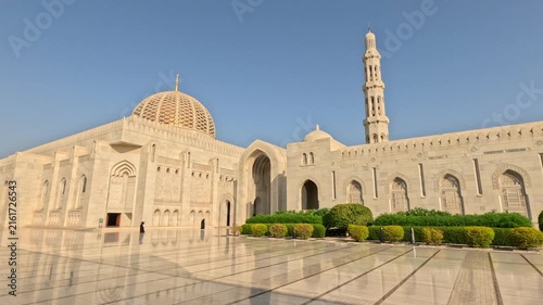 Wide shot of the Sultan Qaboos Mosque in Oman featuring a beautiful white mosque and a glossy polished plaza under a clear sky during daytime.