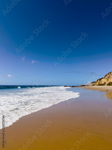 Sandy beach with waves and blue sky 