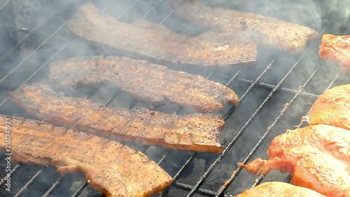 Close-up of seasoned pork belly slices sizzling on hot BBQ grill outdoors with smoke and flames