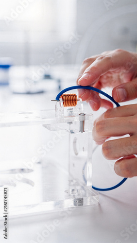 Engineer Assembling Copper Coil Inductor on Acrylic Rig in Laboratory