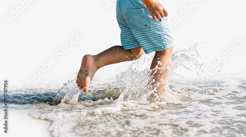 Close up of a childs legs running through shallow ocean water creating splashes on a bright sunny day