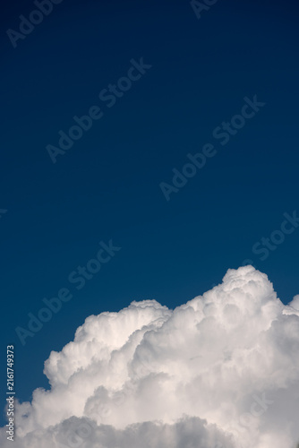 Clear blue sky background with dense white cumulus cloud formation along the bottom. Vertical minimalist cloudscape with generous copy space, crisp lighting, sunny atmosphere, and summer day.