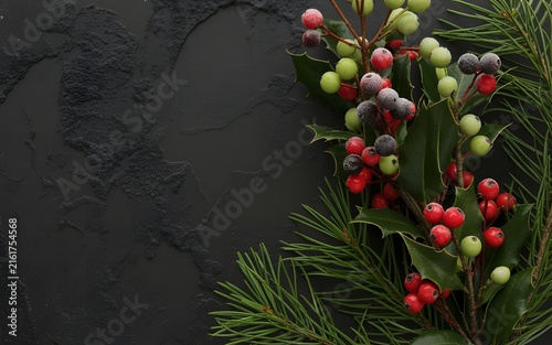 Christmas evergreen branches with red and white berries on dark textured