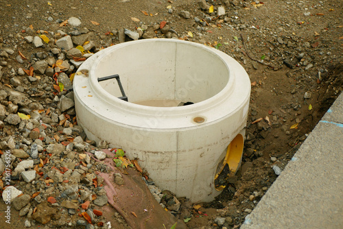 Sewer shaft circular concrete drainage manhole utility installation chamber metal handle or bracket inside structure excavated manhole roadside area soil gravel trench rocks, debris broken stones