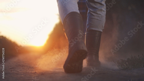 Farmer field corn. Two farmers in rubber boots walk along a farm path at sunset. The farmers carry a pitchfork, and their rubber boots kick up dust on the ground.