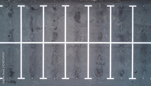 Empty parking lot with white painted lines on dark asphalt surface viewed from a high angle drone aerial perspective shot
