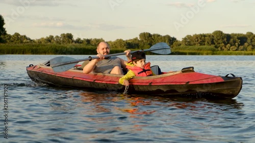 Father and son kayaking together on a calm lake during summer evening sunset.