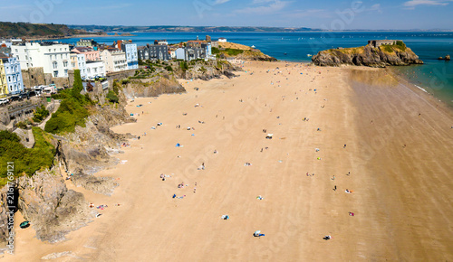 фотографія Wide expanse of sandy shore at low tide below cliffside coastal town, beachgoers