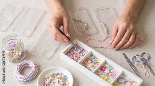 Hands using tweezers to select colorful beads for making a phone charm from a sorted wooden box