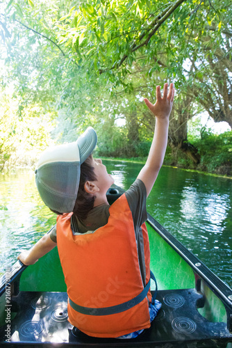 Caucasian child boy, 5 years old, with cap and life jacket, sitting on a canoe trip on Tirino River, in Gran Sasso National Park, located in the Abruzzo region in Italy