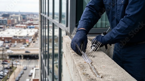 Man exterminator installing anti bird spike on building ledge. Professional pest control worker using adhesive gun to prevent pigeon infestation on city skyscraper exterior balcony safety