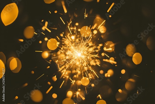 Bright glowing sparkler explosion with golden bokeh light bursts on dark