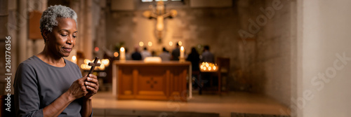Senior Black woman holding a wooden cross in a church. Christian prayer and faith concept. Wide banner with copy space on the right