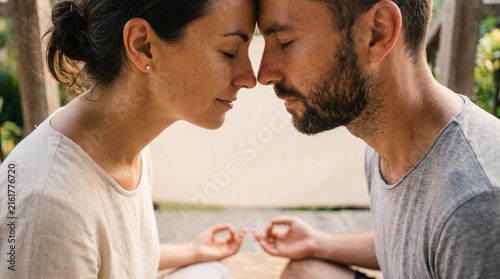 A couple meditates with foreheads touching, eyes closed in peaceful serenity and connection, their hands resting in a meditative mudra, symbolizing spiritual harmony.