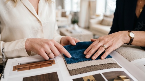 Two women are looking at fabric swatches in a bright, modern showroom, discussing interior design ideas.