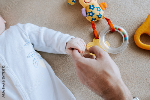  Softly cupped infant toes within caring adult palms. Delicate baby hand cradled tenderly bycexperienced adult hands in soft lighting. Gentle parental contact creates safe haven. 