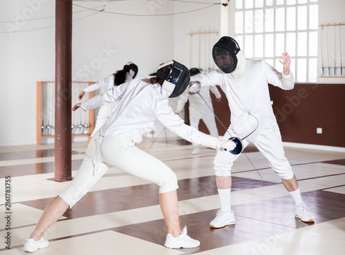 Canvas Print Athletes in protective equipment and helmets conduct a fencing training match in the gym