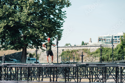 Obraz na plátně Man in a safety helmet assembling a temporary stage structure, preparing for a c