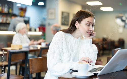 Foto In cozy cafe hall, female freelance works with laptop and drinks coffee