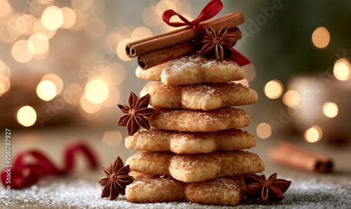 Stacked star-shaped cookies forming a christmas tree, dusted with powdered sugar and cinnamon, decorated with spices and ribbon