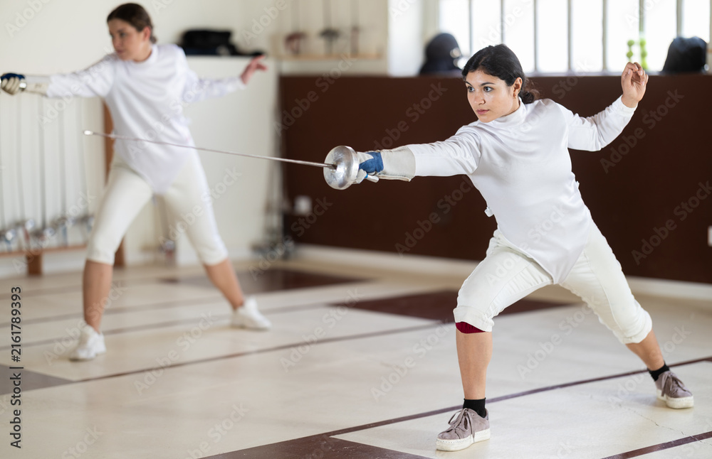 Fototapeta premium Men and women in white uniforms practice fencing techniques with foils in their hands
