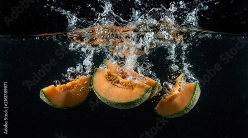 Cantaloupe fruit slices falling into water with bubbles.