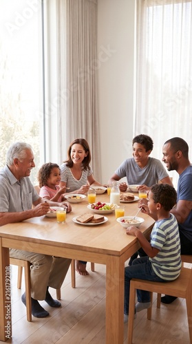 A multi-generational family enjoys a cheerful breakfast around a wooden table, bathed in natural light streaming through a large window.