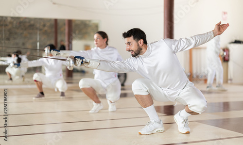 Canvas Print European man in white fencing uniform standing with sword in hand in front of ot