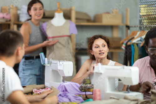 Canvas Print Kind middle-aged female sewer speaking to man and other measuring dummy during s