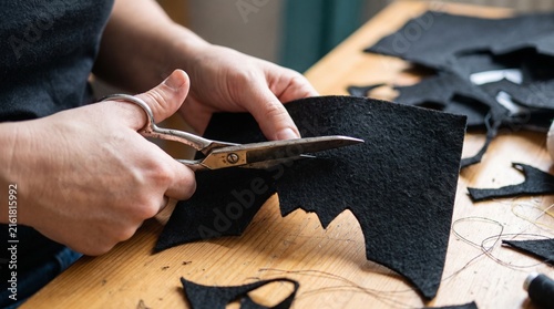 Close-up of hands cutting black felt with scissors to create Halloween decorations. The felt is shaped like a bat with jagged edges.