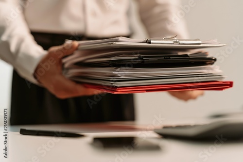 Person holding a stack of papers, files, and folders on a desk
