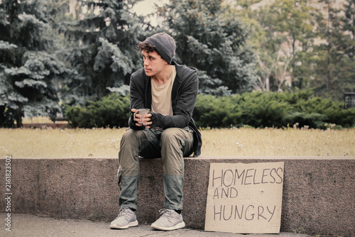 Fotografie Homelessness and poverty crisis, young man sitting with a sign asking for help,