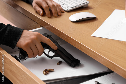 Man taking pistol from desk drawer at office, closeup