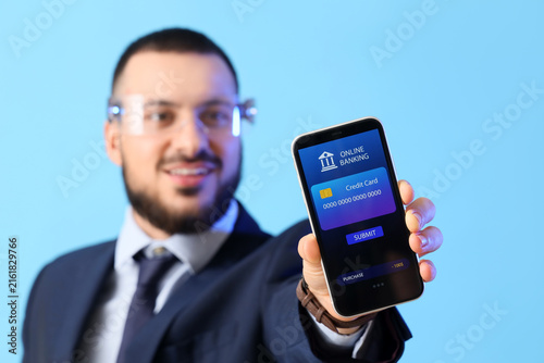 Young businessman in AR glasses with mobile phone on blue background. Online ...