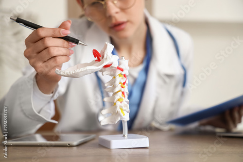 Female medical intern studying spine model at table in clinic, closeup