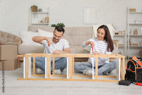 Happy couple with screwdrivers assembling shelf unit at home